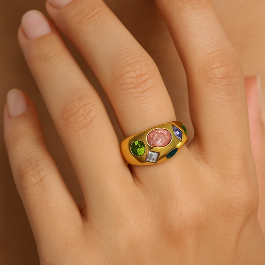 Gold ring with colorful gemstones on a hand against a neutral background