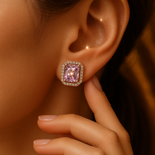 Close-up of a pink gemstone earring worn on an ear with a hand adjusting it.